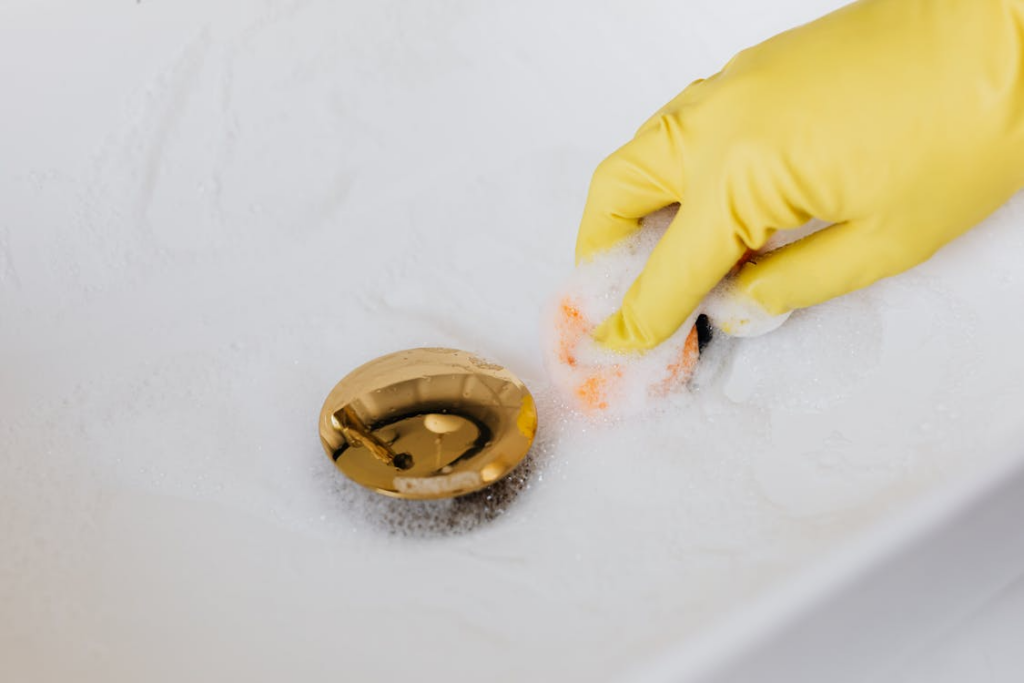A person wearing yellow gloves cleaning the sink.