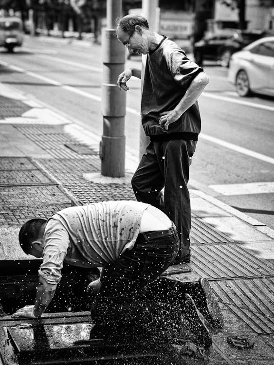 A person standing and another cleaning the sewer.