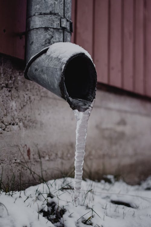 Ice forming around an exposed residential water drain during winter
