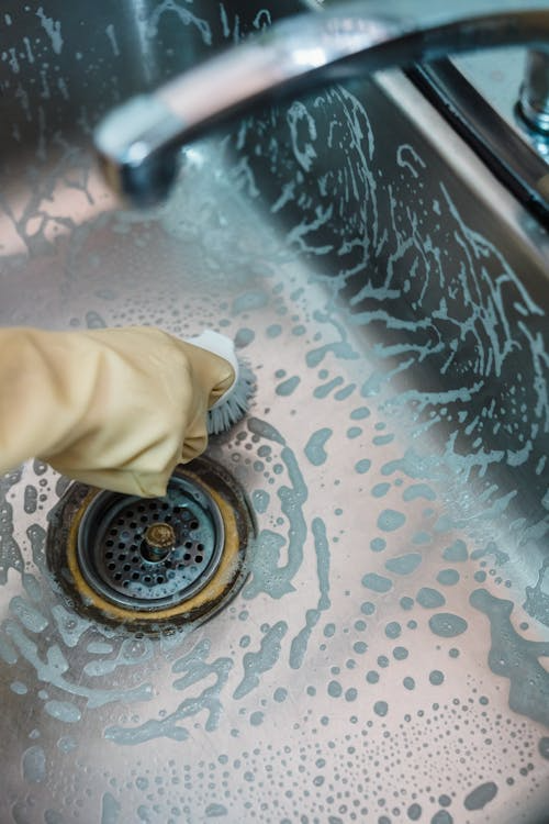 A gloved hand cleaning a sink and drain with a brush