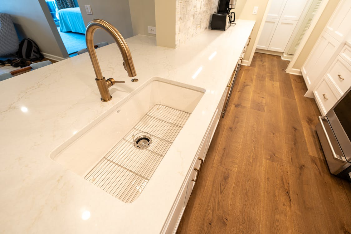 Modern kitchen sink with gold faucet set into a white countertop with built-in drain rack.